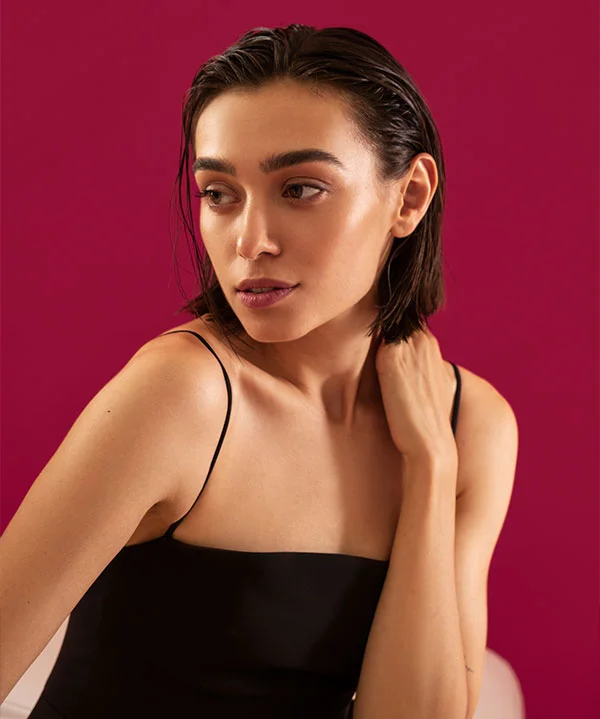 A confident woman posing against a red backdrop, showcasing youthful, radiant skin.