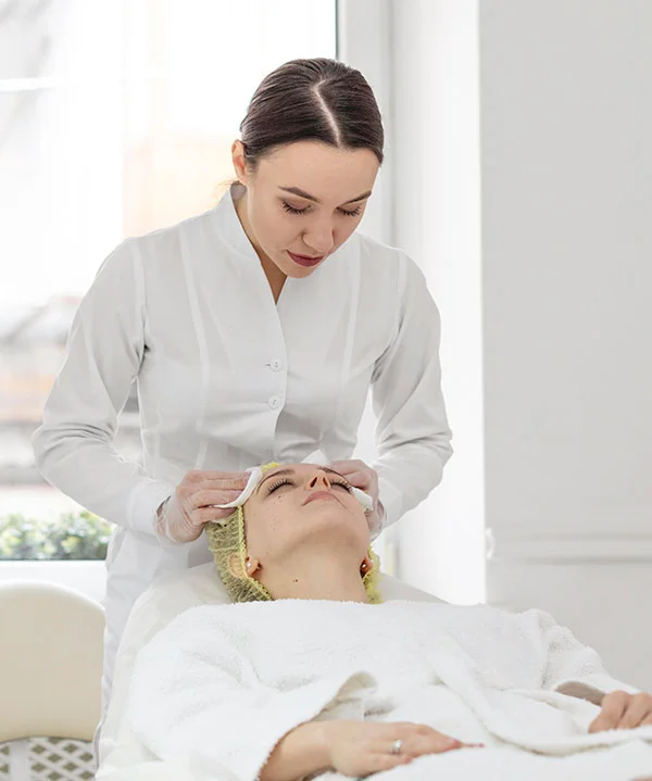 A skincare professional performing a gentle facial treatment on a client in a clean clinic setting.